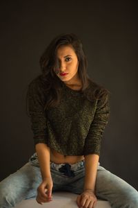 Portrait of beautiful young woman sitting against black background