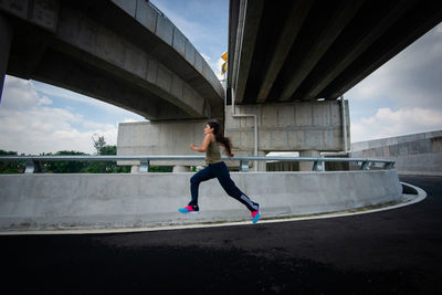 Full length of man skateboarding on bridge in city against sky