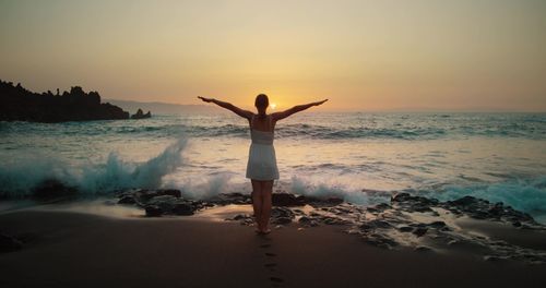 Rear view of woman standing on beach against sky during sunset