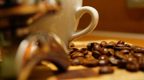 Close-up of roasted coffee beans by cup on table