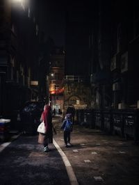 Rear view of people walking on street amidst buildings at night