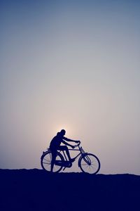 Silhouette person riding bicycle against clear sky