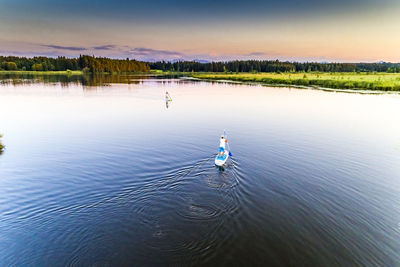 High angle view of friends paddleboarding in lake during sunset