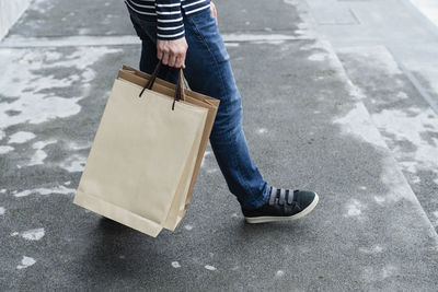 Low section of man with paper bags walking on footpath