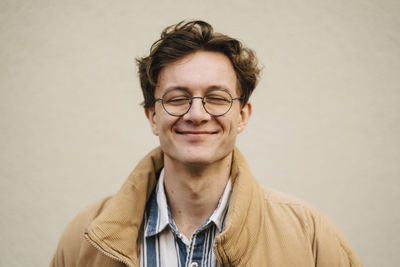 Smiling young man with eyes closed against wall