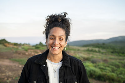 Woman smiling while standing outdoors in nature.