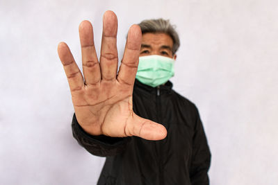 Senior woman in mask gesturing against white wall