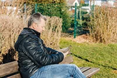 A man sits on a bench in the park and uses a mobile phone to communicate online. communication 