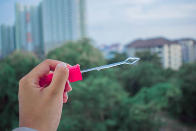 Close-up of hand holding bubble wand against building in city