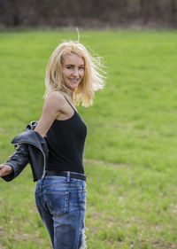 Portrait of smiling woman removing jacket while standing on field