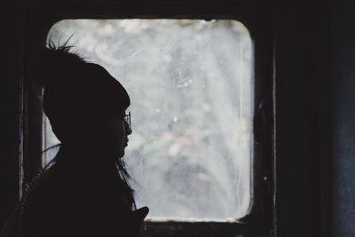 Side view of silhouette woman looking through window