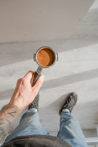 Barista holds in his hand a holder with a tempered coffee tablet for making espresso, tattooed hand