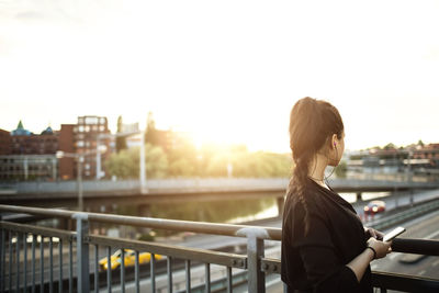 Side view of woman with mobile phone standing on bridge against sky