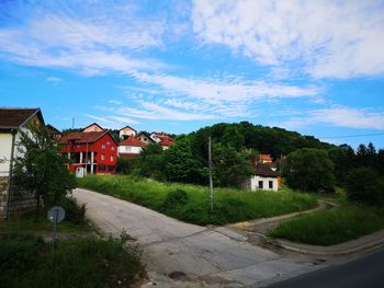 Road amidst houses and buildings against blue sky