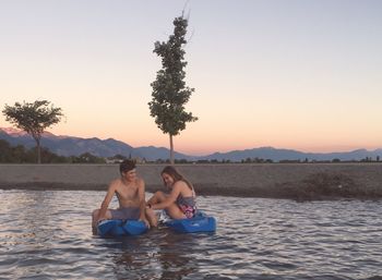 Couple sitting on kayak in sea by trees against sky during sunset at manila creek park