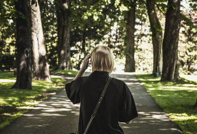Rear view of woman walking on road amidst trees on field