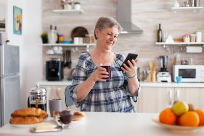 Senior woman holding mobile phone at kitchen