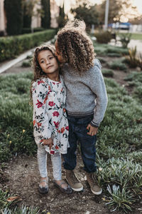 Twin brother kissing sisters cheek while standing outside at park