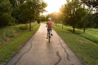 Rear view of young woman riding bicycle on road while wearing a helmet