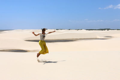 Happy young woman jumping between dunes of lencois maranhenses national park, brazil