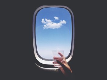 Cropped hand holding drinking glass against airplane window