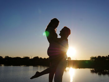 Outline of woman and man standing against lake during sunset