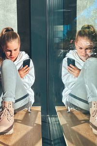  girl sitting at window using mobile phone 