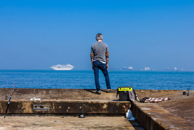 Rear view of man standing on sea against blue sky