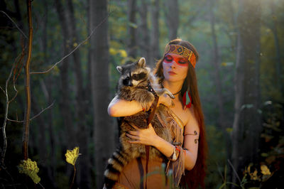 Young woman in traditional clothing carrying raccoon in forest