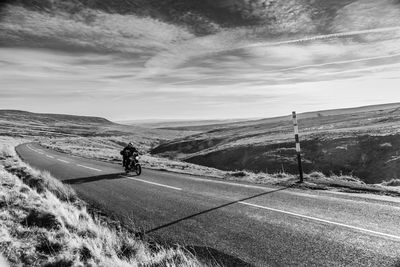 Man riding motorcycle on road by hill against sky