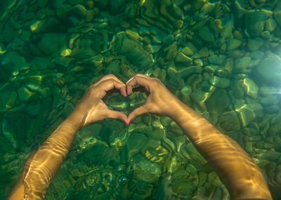 Cropped hands of woman making heart shape in sea