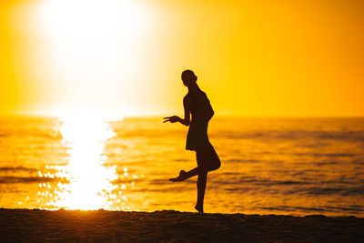 Silhouette woman walking on beach during sunset