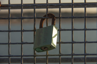 Close-up of metal grate hanging in cage against sky