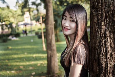 Portrait of a smiling young woman against tree trunk