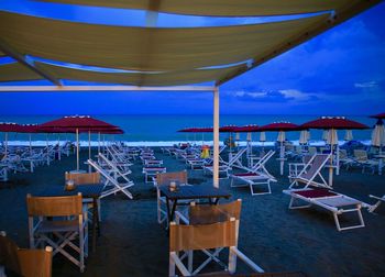 Empty chairs and tables at beach against blue sky