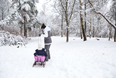 Mom takes his little daughter on a sledge uphill through the winter snow 