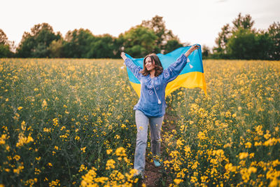 Rear view of woman standing amidst yellow flowering plants on field