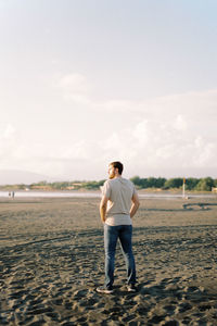 Rear view of man standing on beach against clear sky