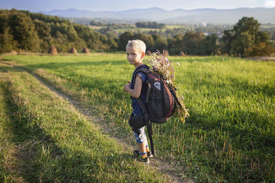 Little hiker with backpack comes from the mountain and carries a bouquet of wildflowers