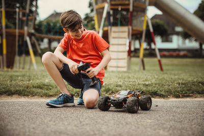 Teen boy with electric remote control car toy play outdoor on sidewalk and have fun while enjoy