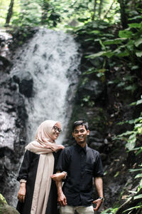 Young couple standing against waterfall at forest