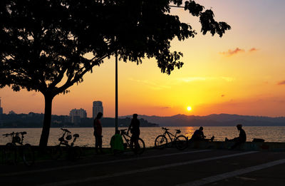 Silhouette people by sea against sky during sunset