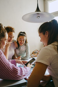 Young woman sharing smart phone with female friends while sitting at table