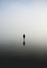 Silhouette of man standing on frozen lake against sky