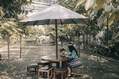 Woman sitting on chair by table against trees