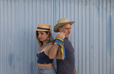 Full length of girl and man wearing hat showing lgbt support against blue wall