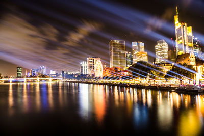 Illuminated city by river against sky at night