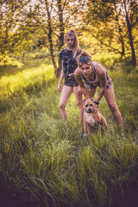 Portrait of friends playing with dog on grassy field at park