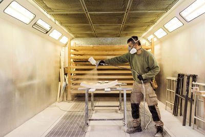 Male carpenter spraying paint on wood material in spraybooth