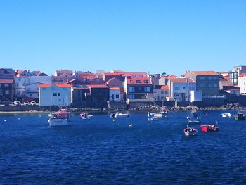 Boats in sea by buildings against clear blue sky